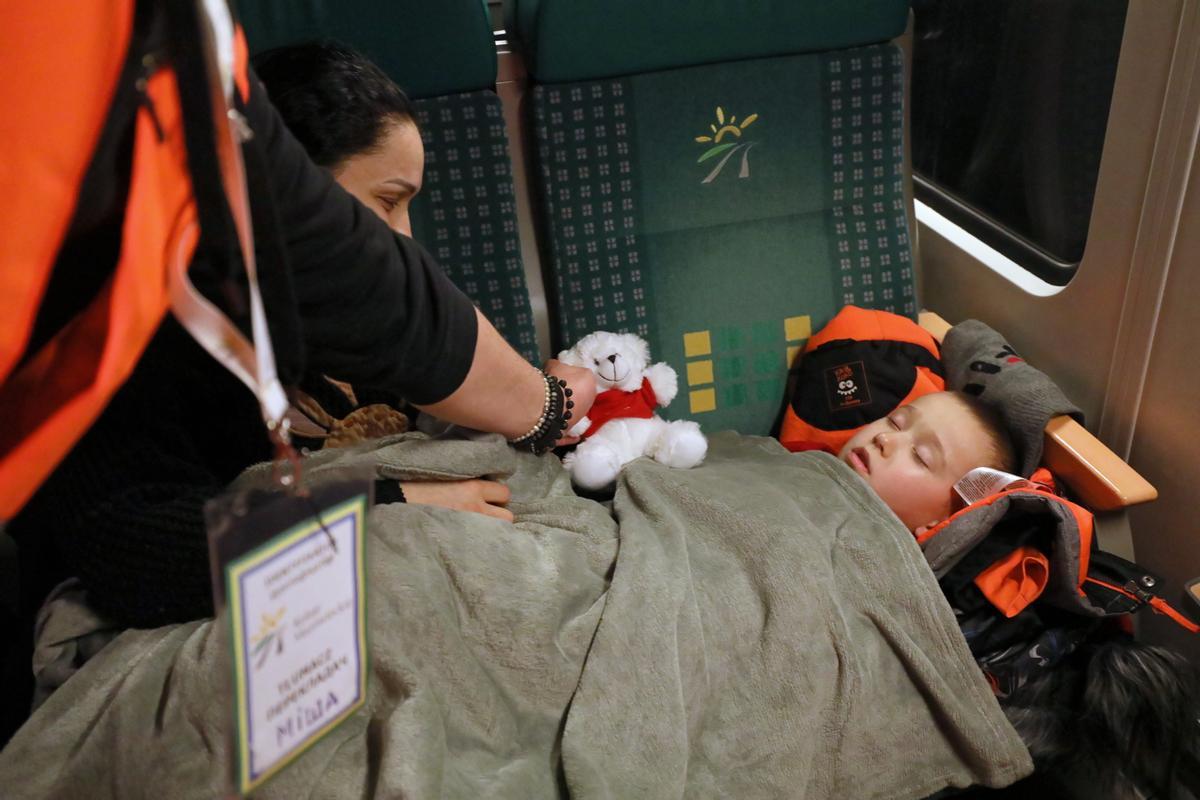 Un asistente acerca un osito a un niño dormido en el tren, a su llegada a la estación de Varsovia Este, en Polonia.