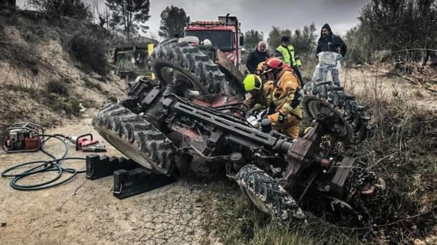 Los bomberos trabajando para liberar el cuerpo del fallecido, atrapado debajo del tractor.