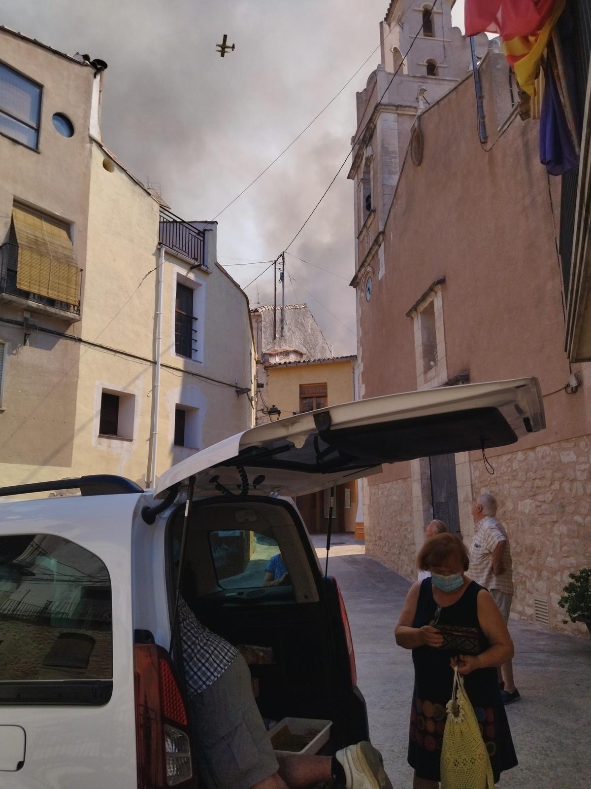 Una vecina compra el pan mientras un avión de extinción sobrevuela el pueblo