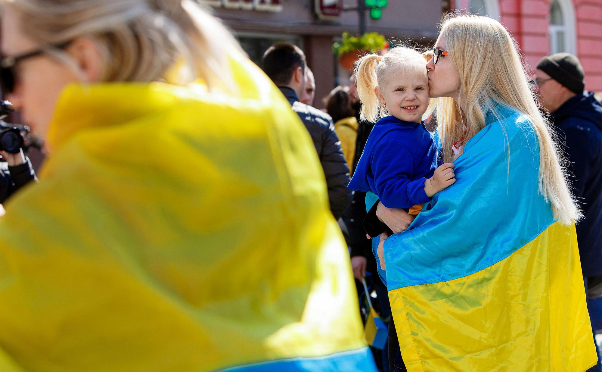 Una mujer arropada por una bandera de Ucrania besa a una niña durante una manifestación.