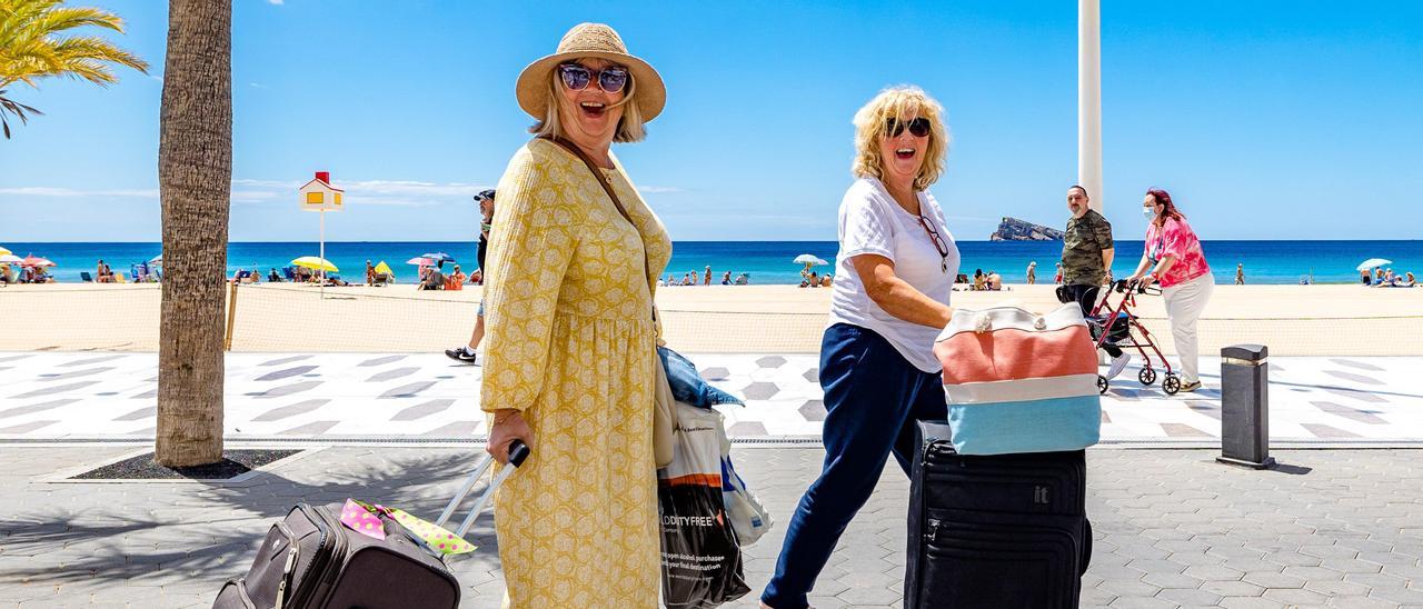 Dos turistes caminen pel passeig marítim de Benidorm en direcció al seu hotel