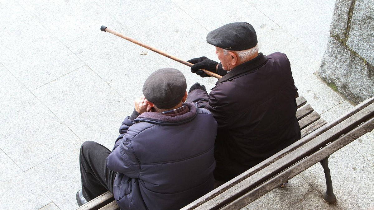 Dos ancianos conversan sentados en un banco.