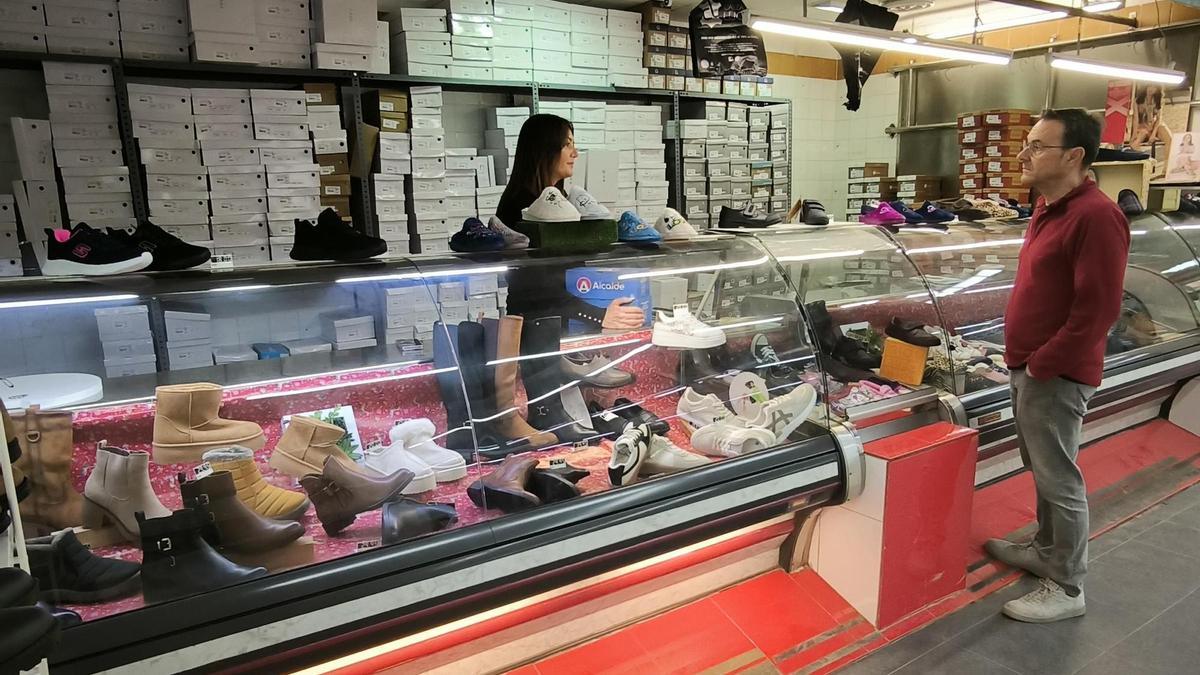 Una mujer atiende a un cliente en una zapatería que tuvo que ser trasladada al mercado de Benetússer