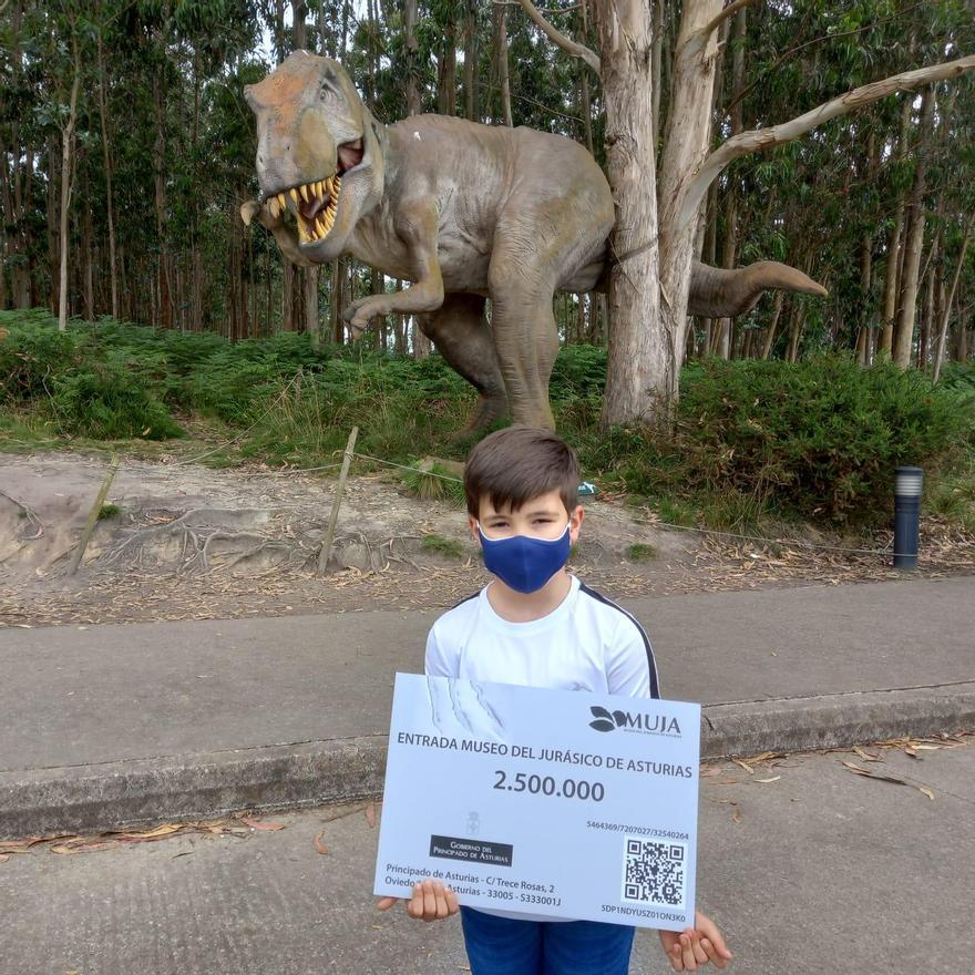 El pequeño, con su diploma, posa delante de una recreación de un dinosaurio.