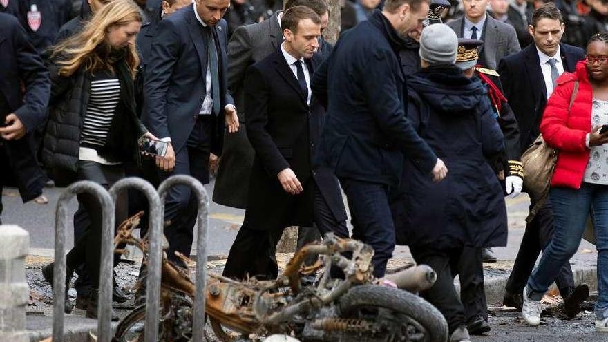 Macron pasa junto a una moto calcinada en su recorrido de ayer por París para evaluar los daños. // Efe