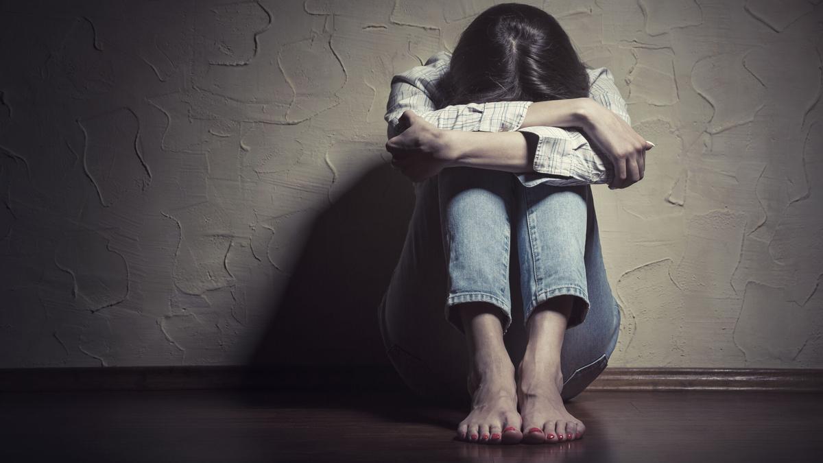 Una mujer cabizbaja, sentada en el suelo de una habitación.
