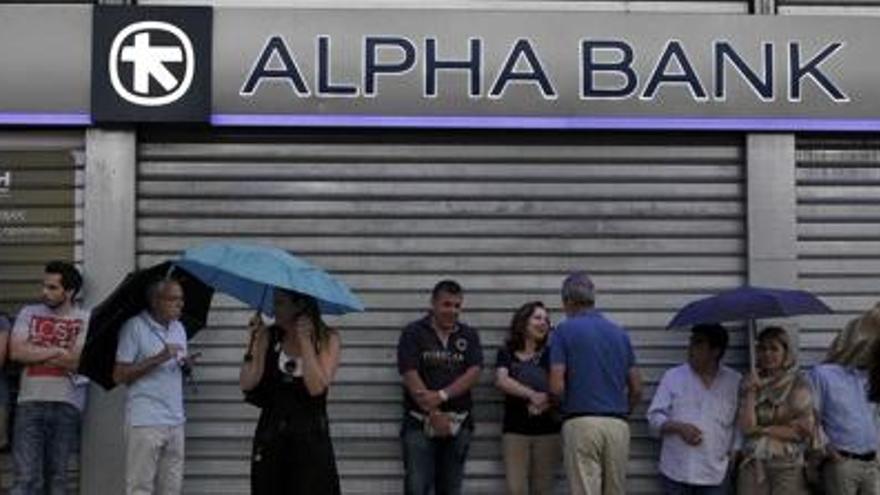 Ciutadans grecs fan cua davant d&#039;un banc, tancat, a l&#039;espera de poder treure diners del caixer automàtic.
