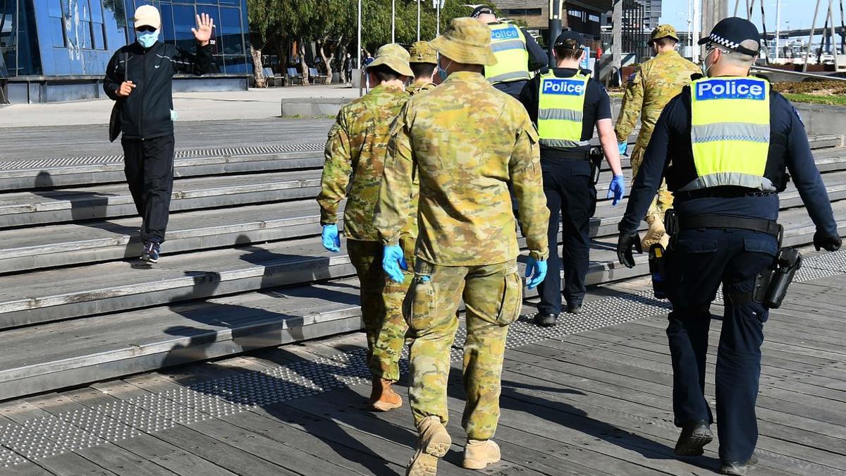 Un hombre saluda a un grupo de soldados y policías tras decretarse el toque de queda nocturno en Melbourne por covid-19.