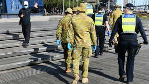 Un hombre saluda a un grupo de soldados y policías tras decretarse el toque de queda nocturno en Melbourne por covid-19.