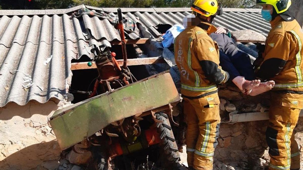 Los bomberos evacúan a uno de los heridos. Se ve el boquete que el tractor ha abierto en la casa