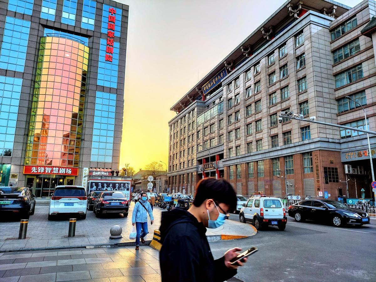 Un joven camina por una céntrica calle de Pekín mirando el móvil