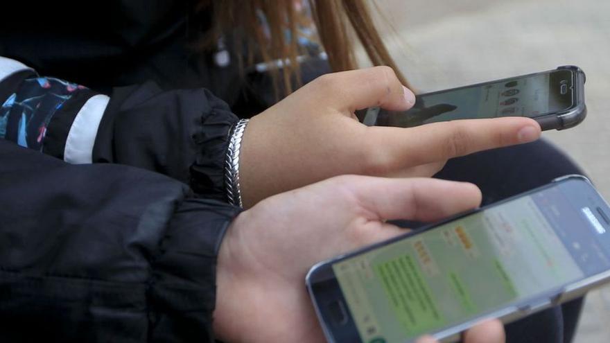 Dos jóvenes consultan sus teléfonos móviles en la calle.