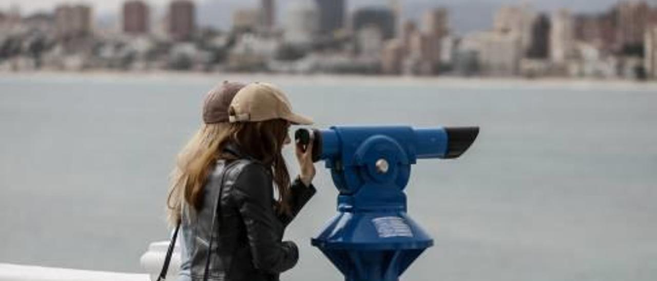 Una turista mira a través de uno de los telescopios instalados en la zona del Castillo hacia la playa de Poniente.