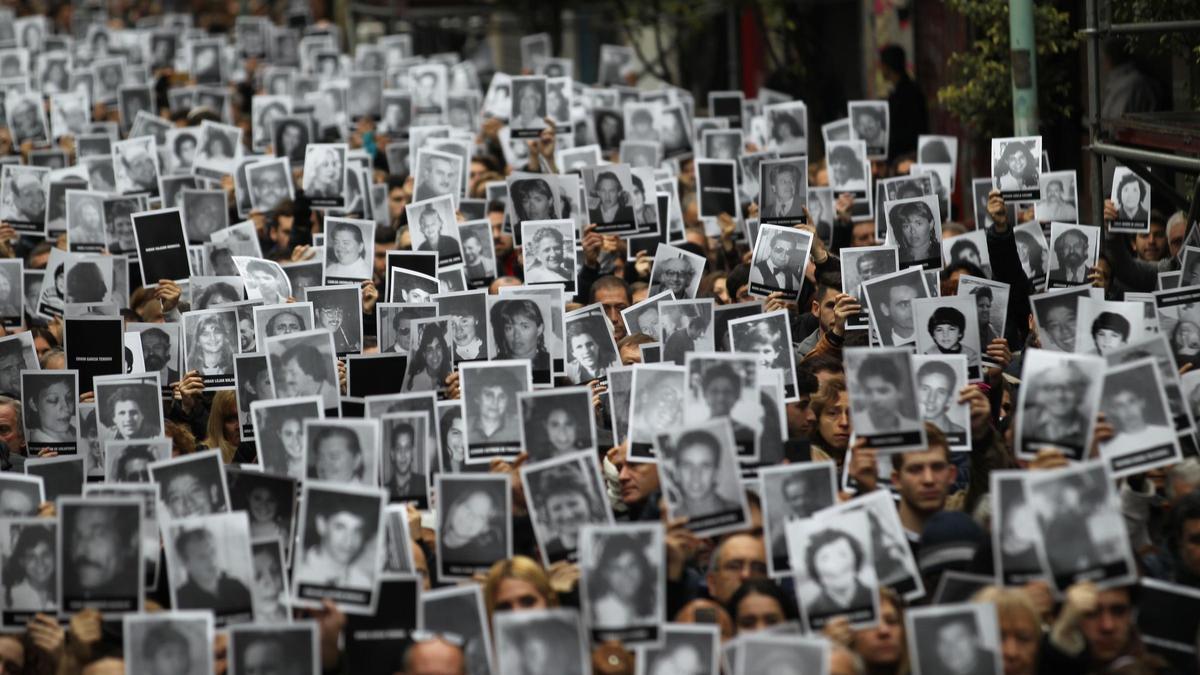Cientos de personas levantan las fotografías de las 85 víctimas del atentado contra la mutua AMIA de Buenos Aires, en una concentración en 2018.