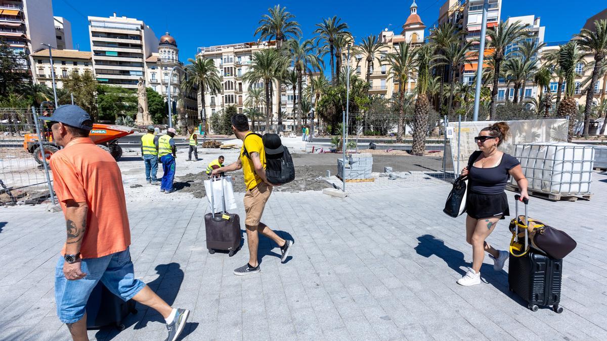 Varios turistas pasan frente a las obras en el frente litoral de Alicante, este lunes.