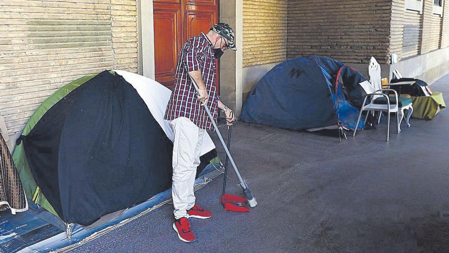 Santi limpia los porches en los que llevan viviendo un año en el llamado Campamento de la Justicia.