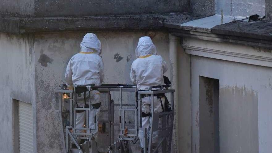 Dos bomberos retiran un nido de velutinas bajo el voladizo de un edificio.