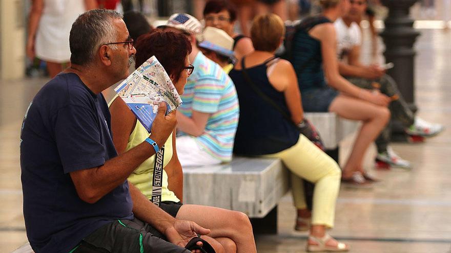 Un hombre se abanica con un mapa en la calle Larios.