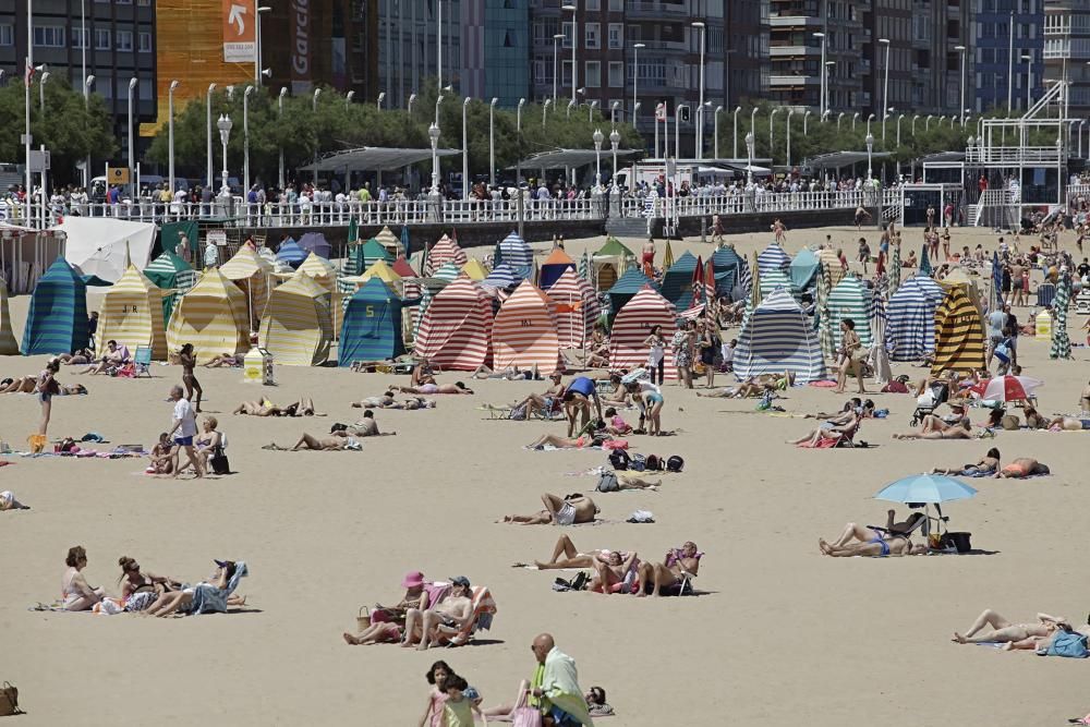 Gijoneses y visitantes se lanzan a la playa en una jornada calurosa.