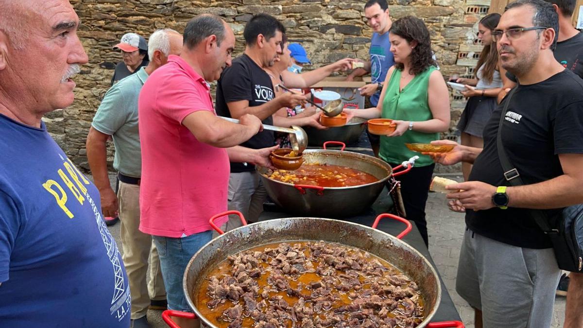 Reparto del guiso de ternera y patatas. A la derecha, los comensales llenan la Plaza Mayor de Rabanales. |  Chany Sebastián