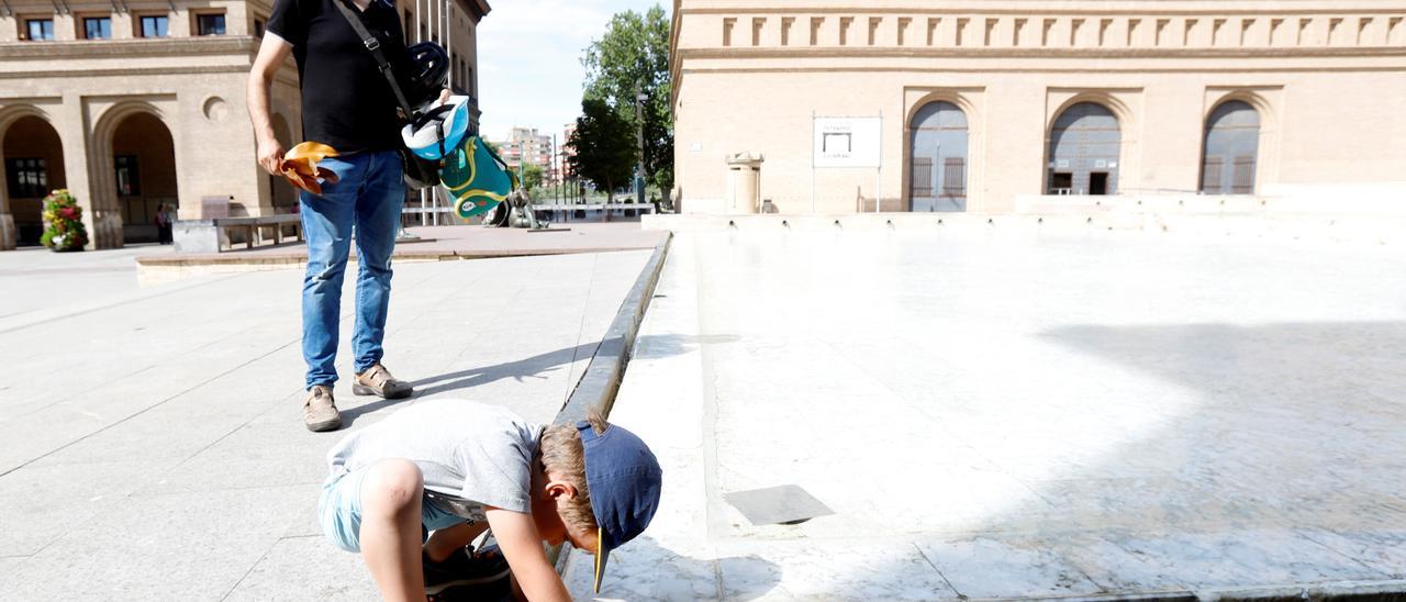 Un niño se refresca en la fuente de Goya, en la plaza del Pilar, bajo la atenta mirada de su padre, ayer.