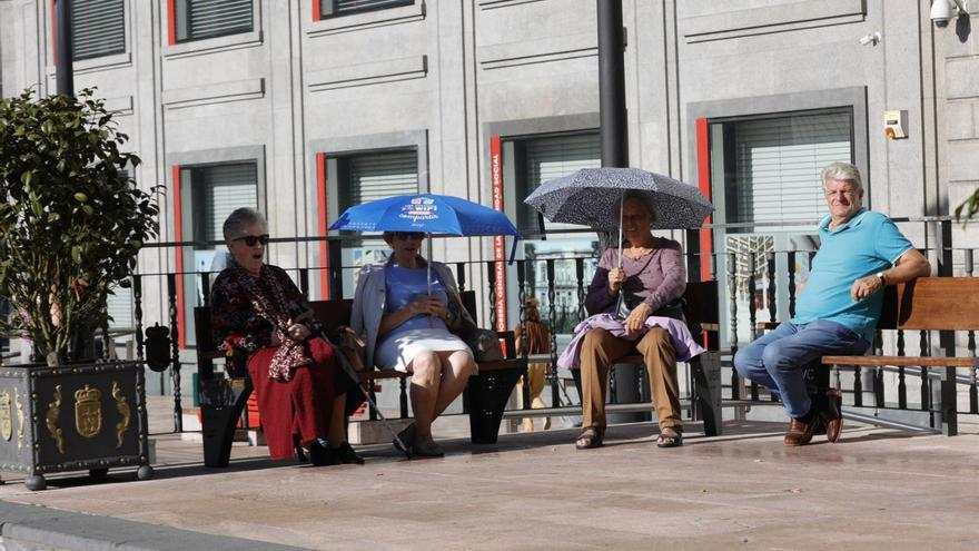 Mujeres, resguardándose del sol con paraguas, este jueves, en la plaza de la Escandalera de Oviedo. | Miki López