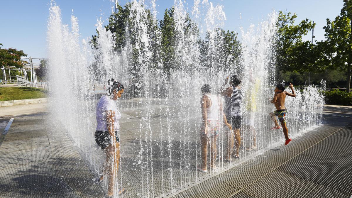 Un grupo de jóvenes combate el calor y se refresca en una fuente de la Expo de Zaragoza.