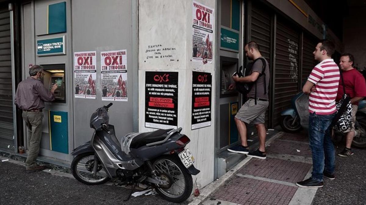 Colas ante cajeros en Atenas, con carteles a favor del 'no' en el referendum