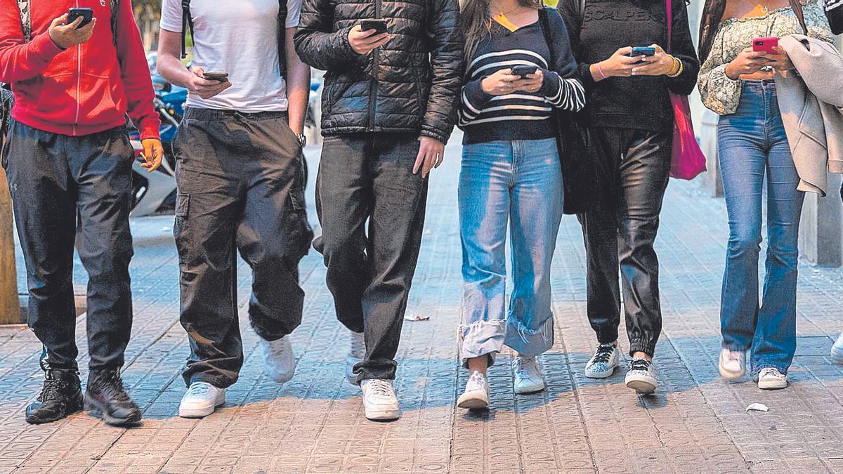 Jóvenes atentos a las pantallas de sus móviles a la salida del instituto
