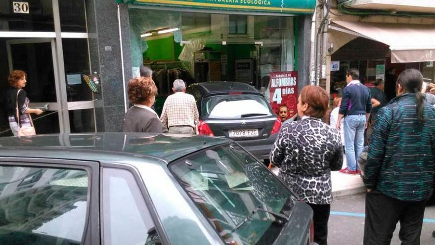 Numerosas personas que pasaban por la zona observan el coche estampado en la tintorería.