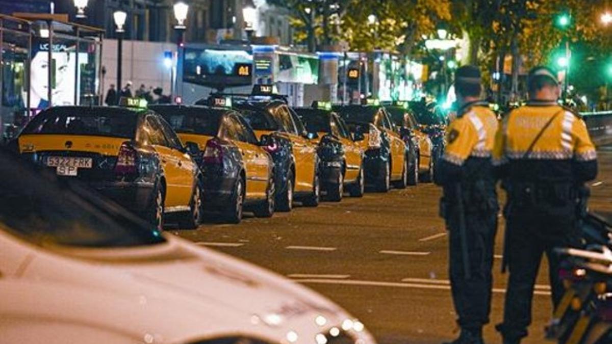 Cola de taxis y una patrulla de la Guardia Urbana, el lunes por la noche en una de las paradas situadas en la plaza de Catalunya.