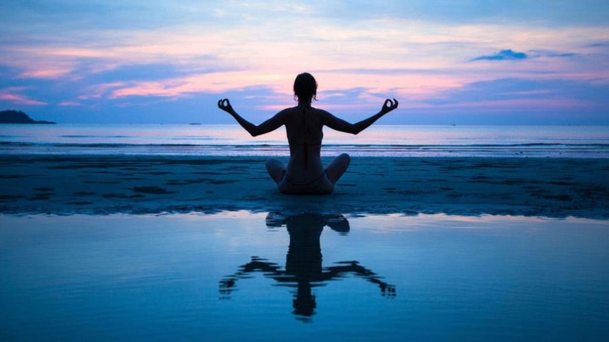 Una mujer practica yoga al atardecer en una playa de Canarias.