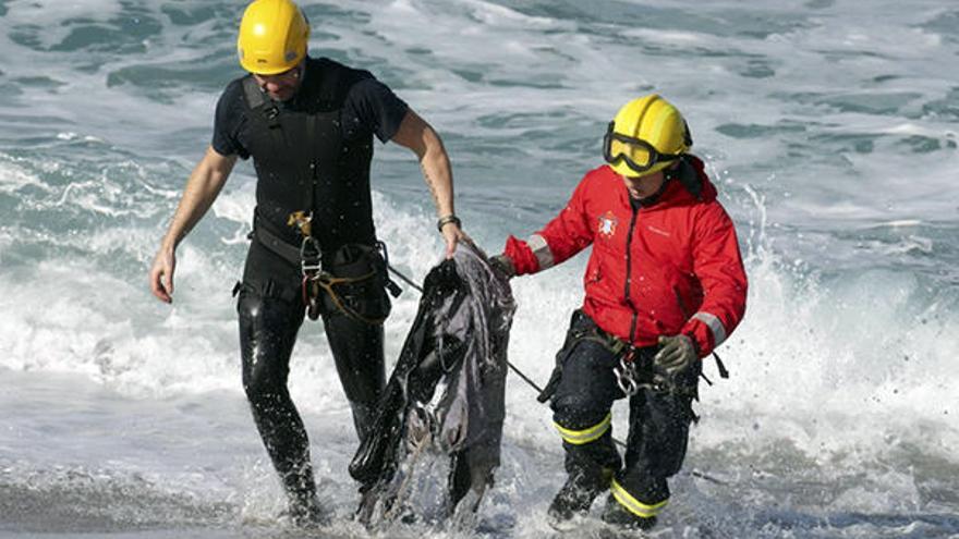 Miembros del cuerpo de bomberos de A Coruña retiran restos de ropa de la playa del Orzán