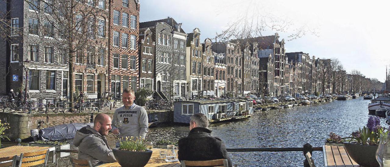 Varios jóvenes disfrutan de unos vinos en los canales de Amsterdam.