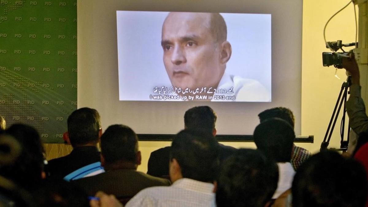 Unos periodistas observan la imagen de Jadhav mientras el portavoz del ejército paquistaní explcia su condena.