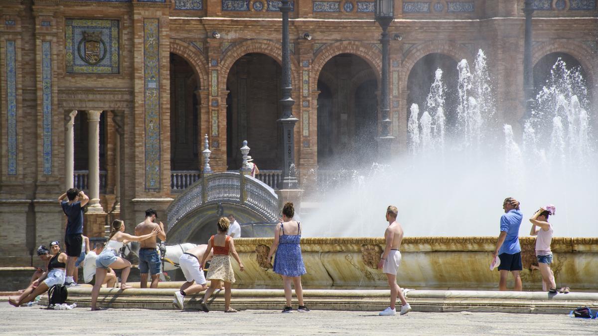 Varios turistas se refrescan en la fuente de la Plaza de España de Sevilla.