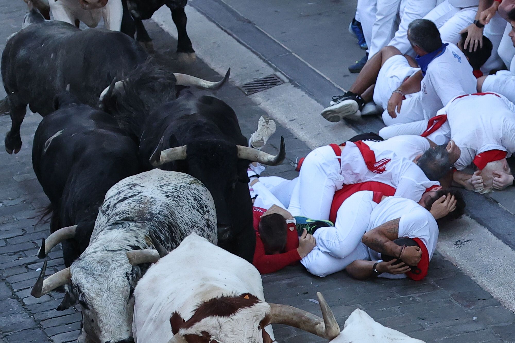 PAMPLONA, 08/07/2025.- Varios corredores se protegen tras caer al paso de los toros de la ganadería Cebada Gago durante el segundo encierro de los Sanfermines este martes, en Pamplona. EFE/ J.P. Urdiroz