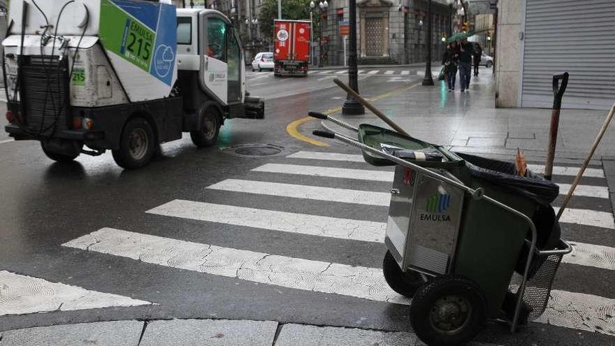 Un camión de limpieza de Emulsa, en una calle céntrica de Gijón, junto a un carrito de barrendero.