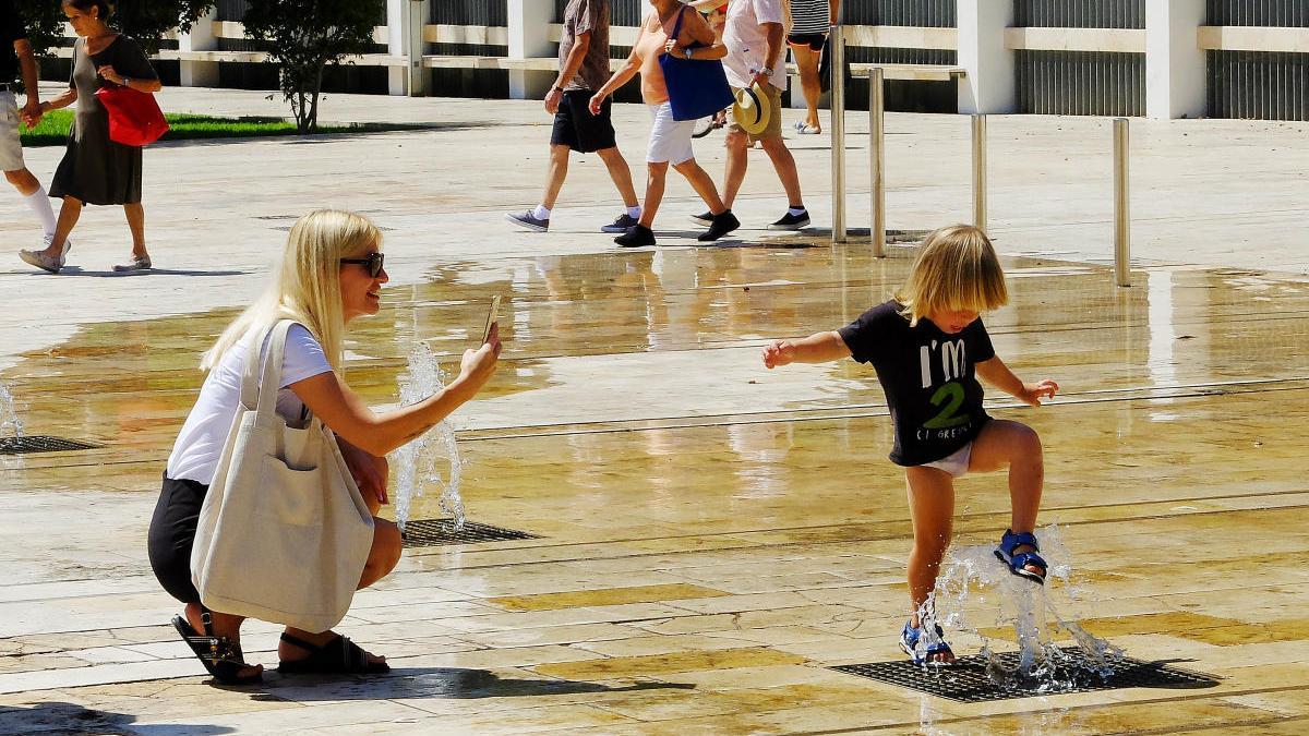 Una madre fotografía a su hija mientras juega y se resfresca en una fuente de Elche. ANTONIO AMORÓS