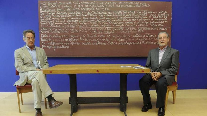 Xosé y Camilo Díaz Arias posan en una reciente exposición ante un panel con las normas de las fábricas de Sargadelos escrito por su padre.