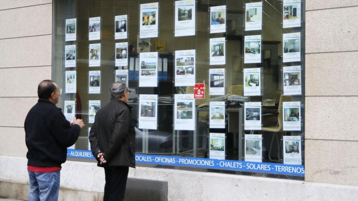 Dos hombres ven anuncios de pisos en una inmobiliaria de Vigo.
