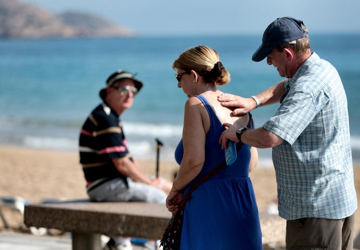 Un señor le aplica crema solar a una mujer en la espalda en una playa de Alicante.