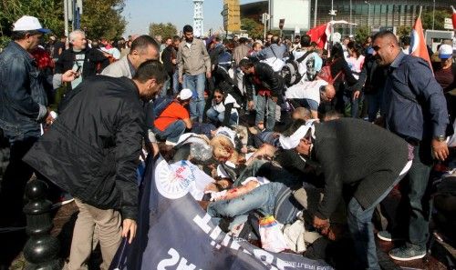 People lay on the ground as survivors surround them to offer help after an explosion during a peace march in Ankara