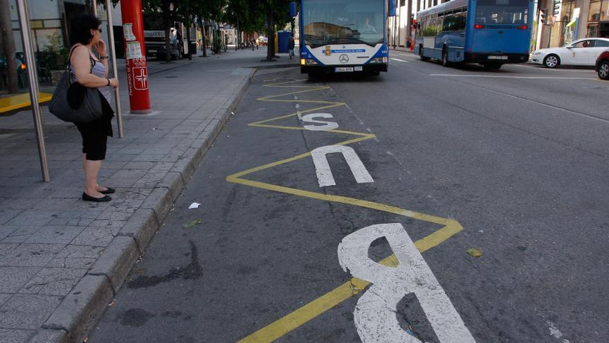 Una mujer espera la llegada del bus en una marquesina de Avilés.