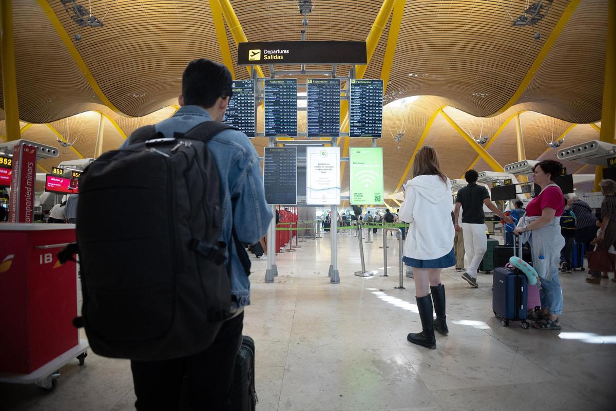 Viajeros delante de las pantallas de aviso de vuelos en el aeropuerto de Madrid.