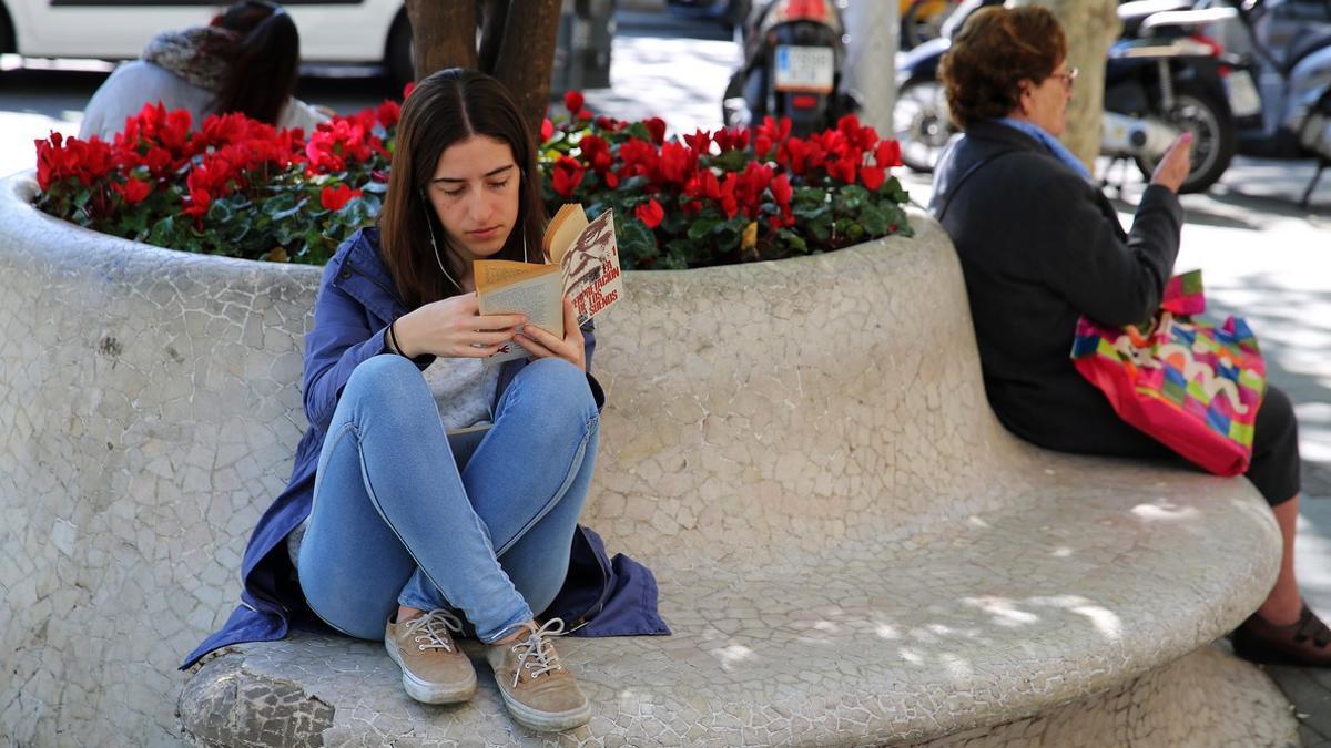 Una joven disfruta de la lectura en soledad, en un banco del paseo de Gràcia, en Barcelona.