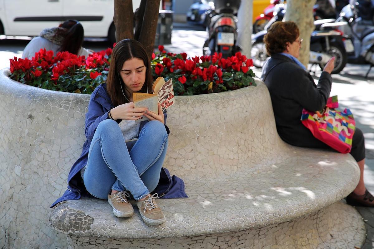 Una joven disfruta de la lectura en un banco del paseo de Gràcia de Barcelona.