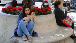 Una joven disfruta de la lectura en un banco del paseo de Gràcia de Barcelona.