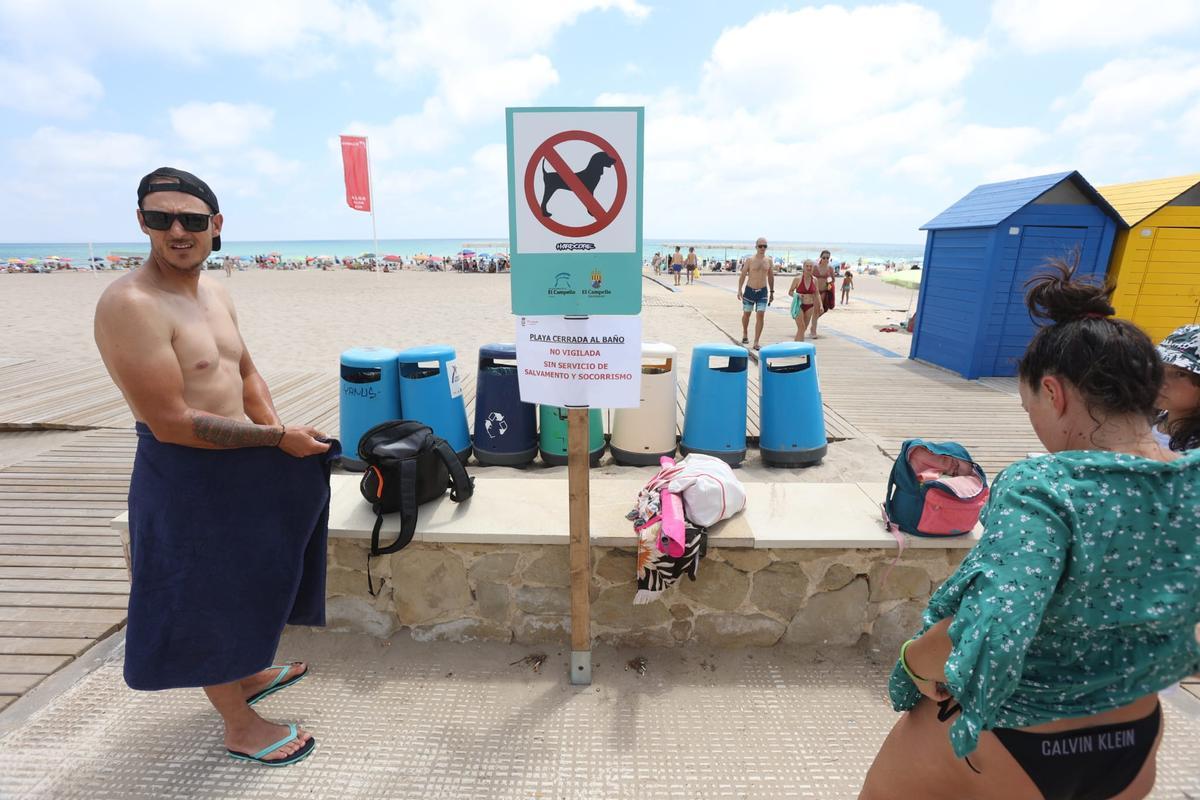 Unos bañistas se secan frente al cartel informativo que se encontraba en los accesos a las playas.