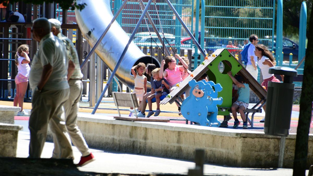 Dos personas mayores paseando ayer por el centro de Cangas al lado de un parque infantil con niños.